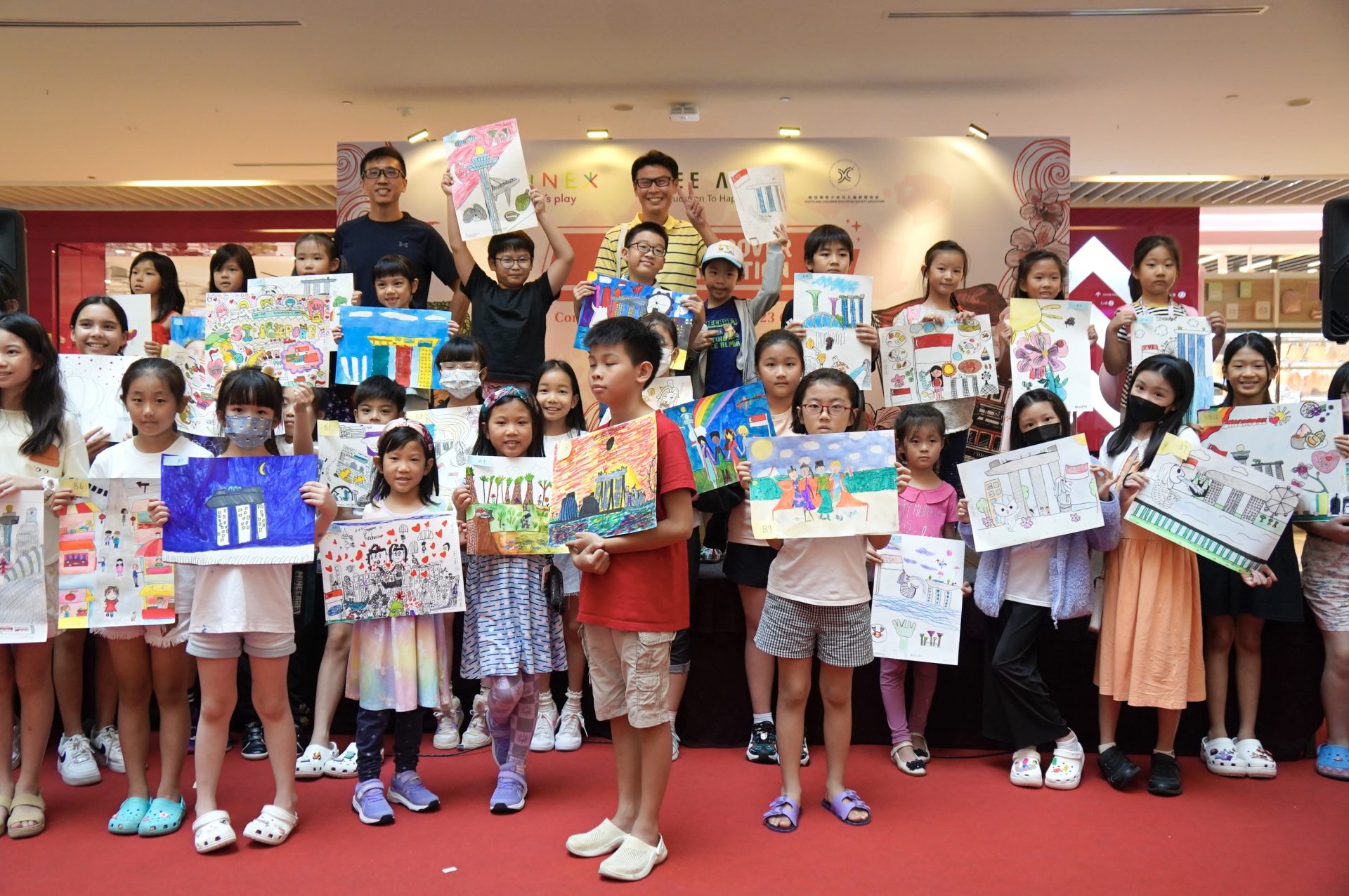 Dozens of young artists holding up their Singapore-themed paintings at the Kine-x CultuRediscover prize ceremony